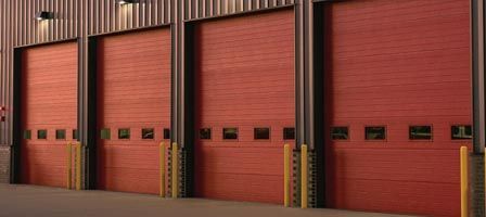 Three large red industrial doors with safety bollards.