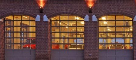 Three arched garage doors, with glass windows, lit from above, and red brick facade.