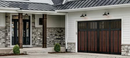 House exterior with stone and wood accents, dark wood garage door, and metal roof.