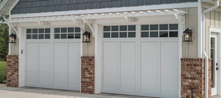 White garage doors with brick columns and a white pergola.