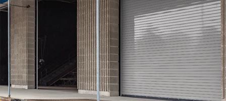 Building facade with a dark interior entrance and a closed metal shutter.
