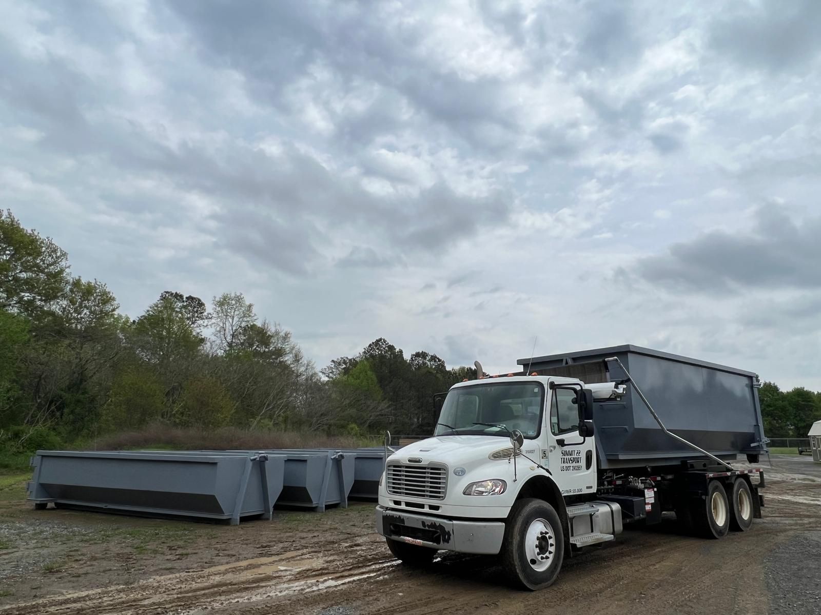 A dump truck is parked on the side of the road next to a row of dumpsters.
