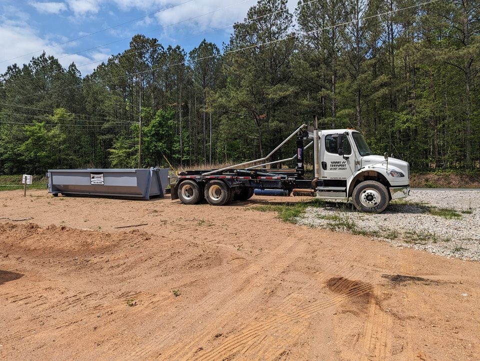 A dump truck is pulling a dumpster in a dirt field.