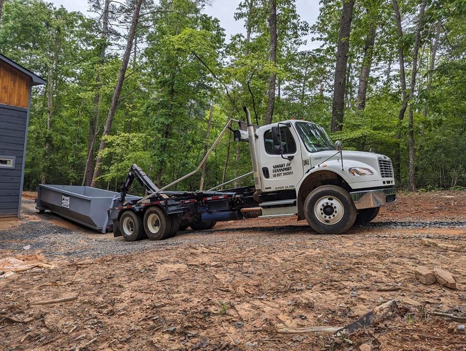 A dump truck with a dumpster attached to it is parked in a dirt field.