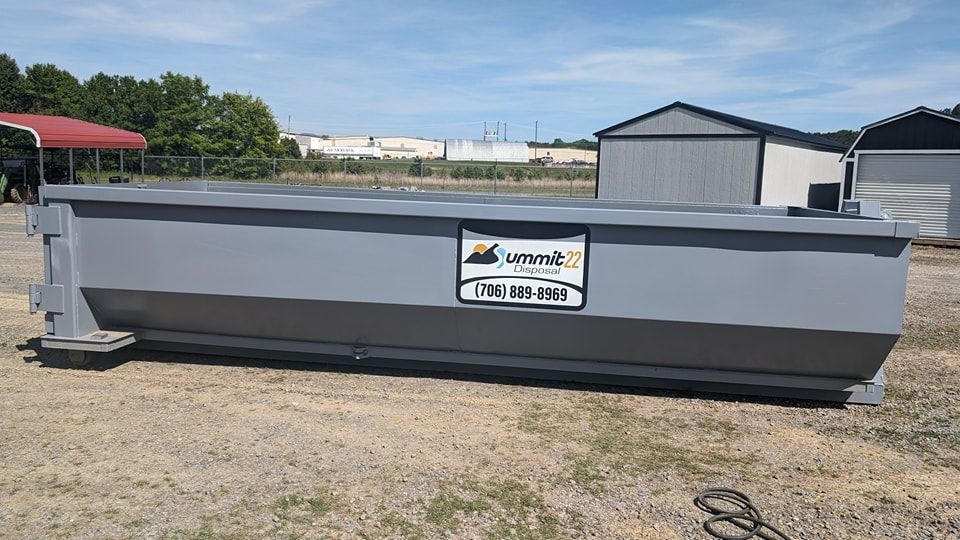 A large gray dumpster is sitting on top of a dirt field.