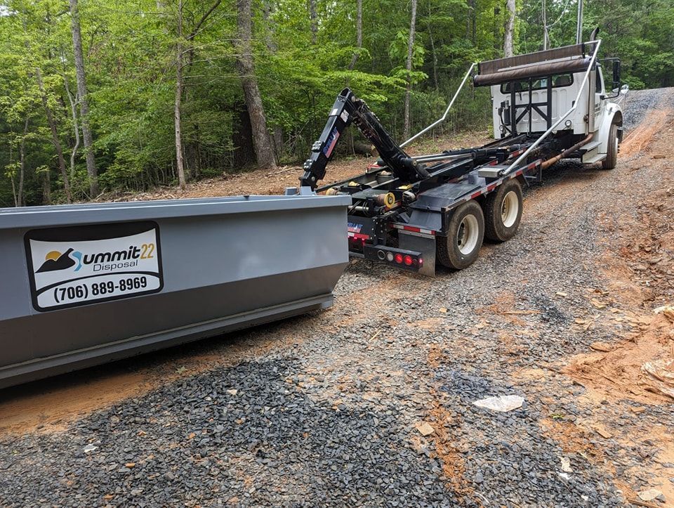 A dumpster is being towed by a dump truck on a dirt road.