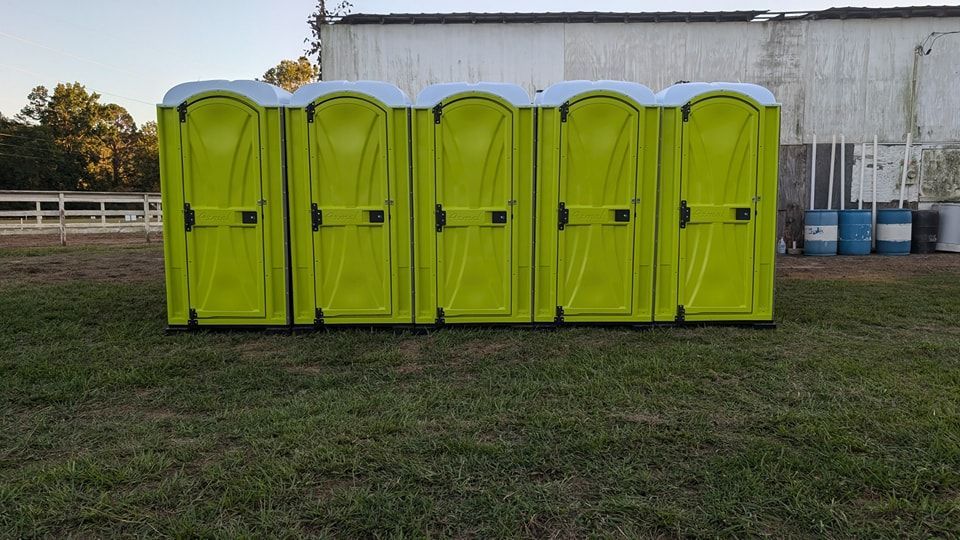 A row of green portable toilets are lined up in a grassy field.