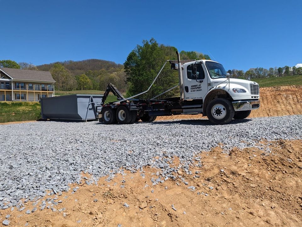 A dump truck is driving down a gravel road next to a house.