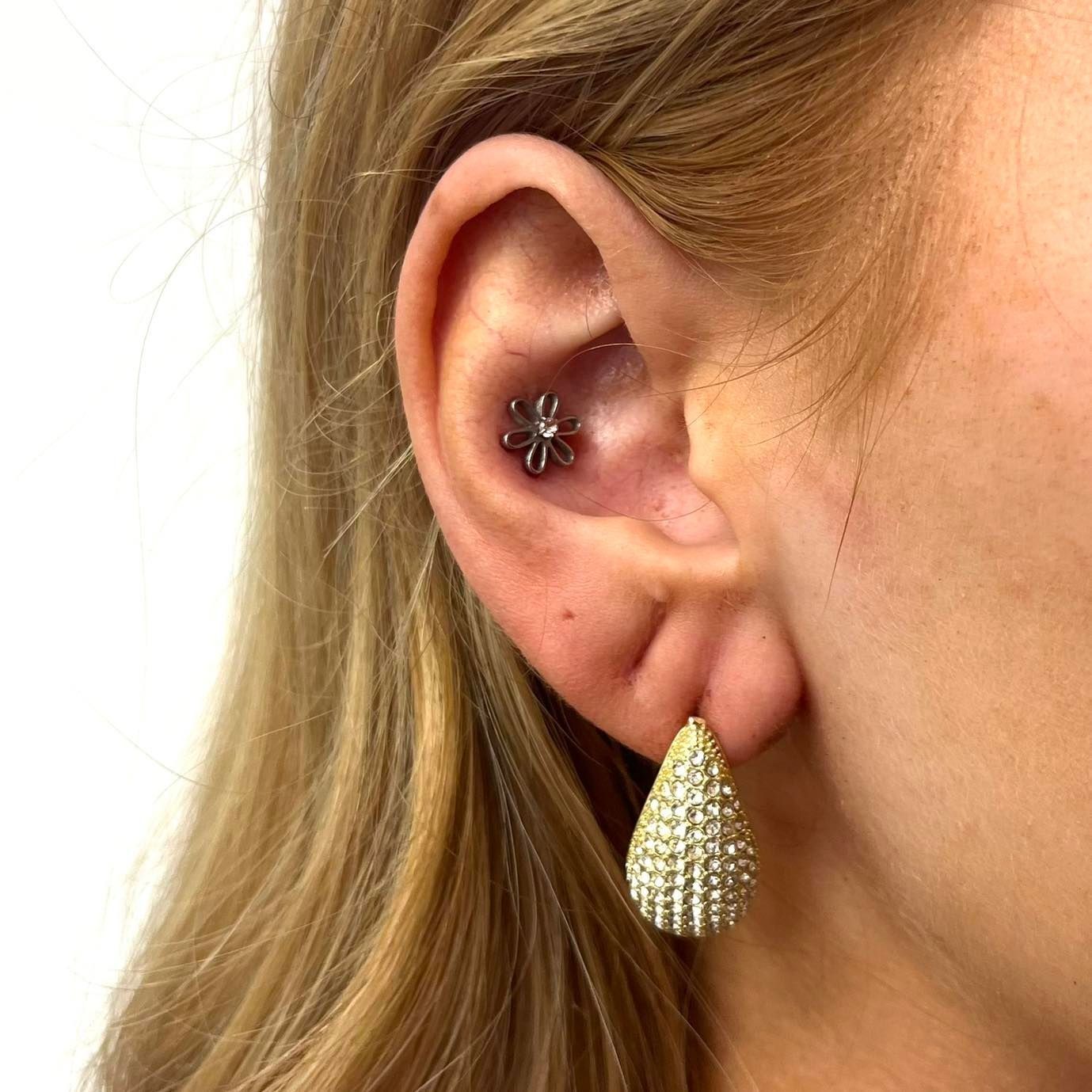Close-up of a woman's ear with a tragus piercing and a teardrop-shaped, jeweled earring.