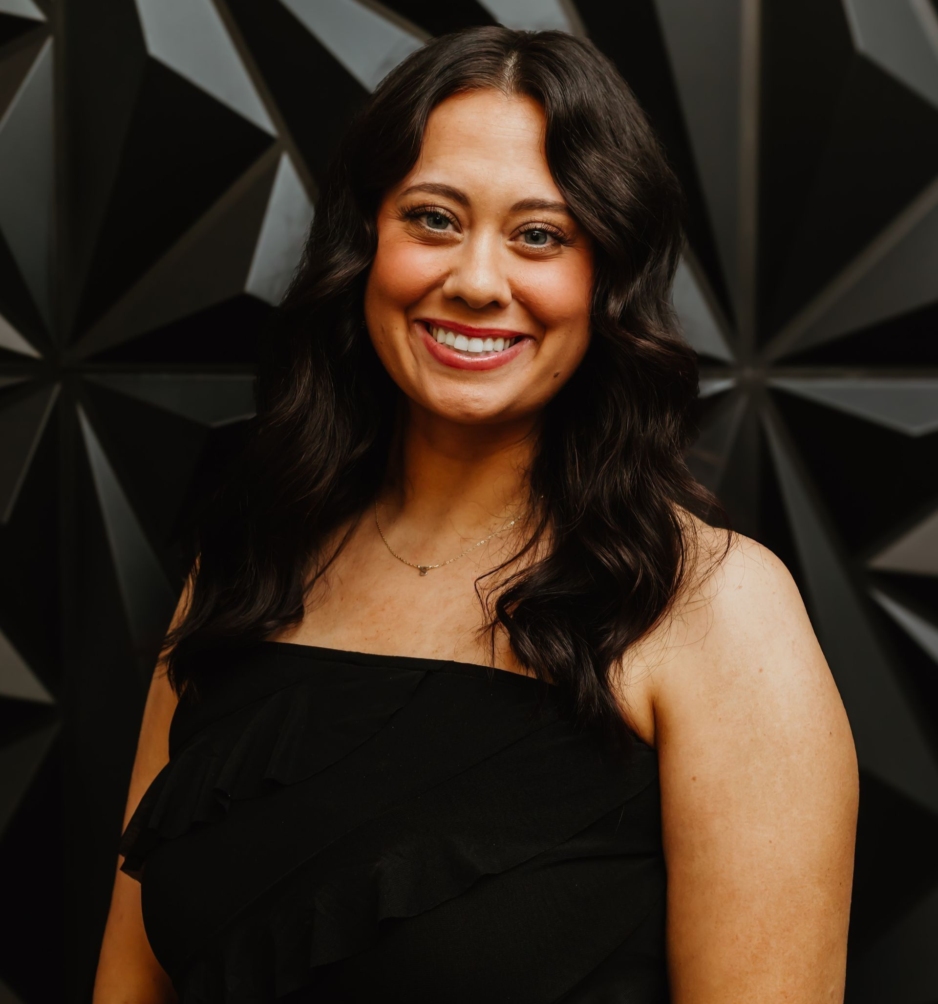 Woman with dark hair smiles, wearing a black, strapless top