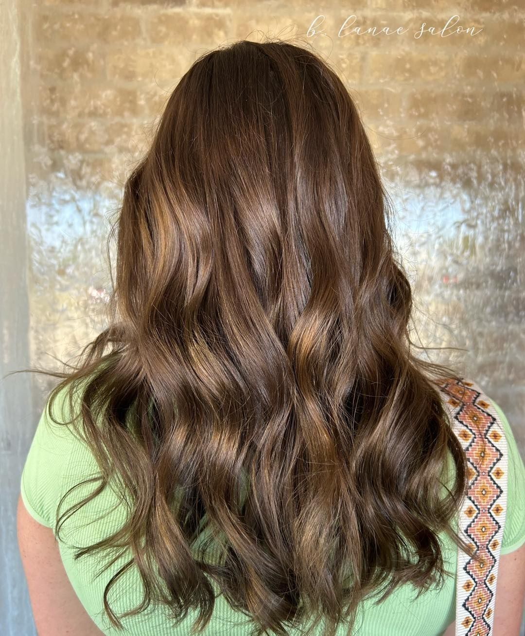 Woman with wavy, brown hair; wearing green top, tan-colored highlights.