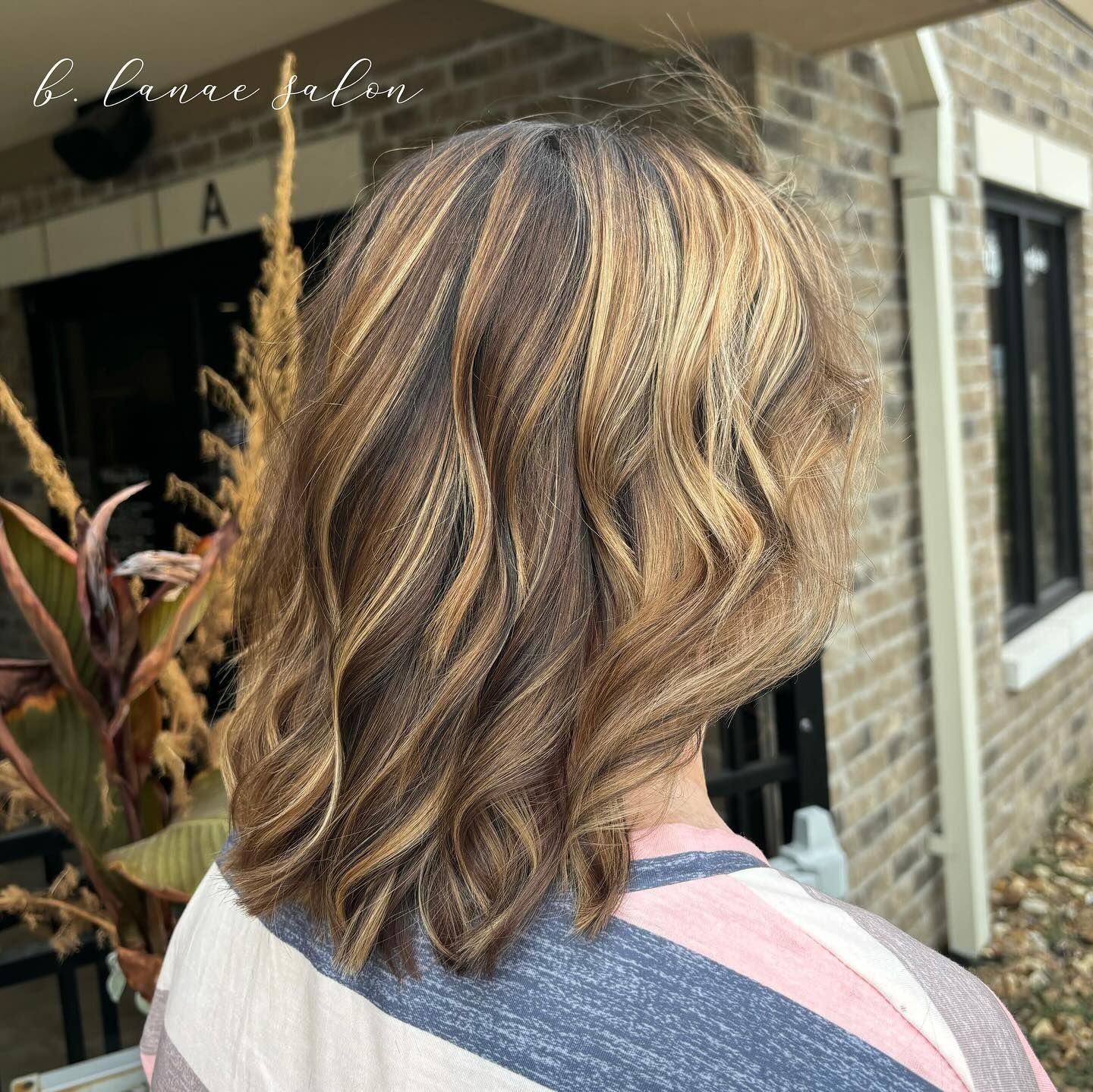 Woman with shoulder-length hair styled with highlights, standing outside a salon.