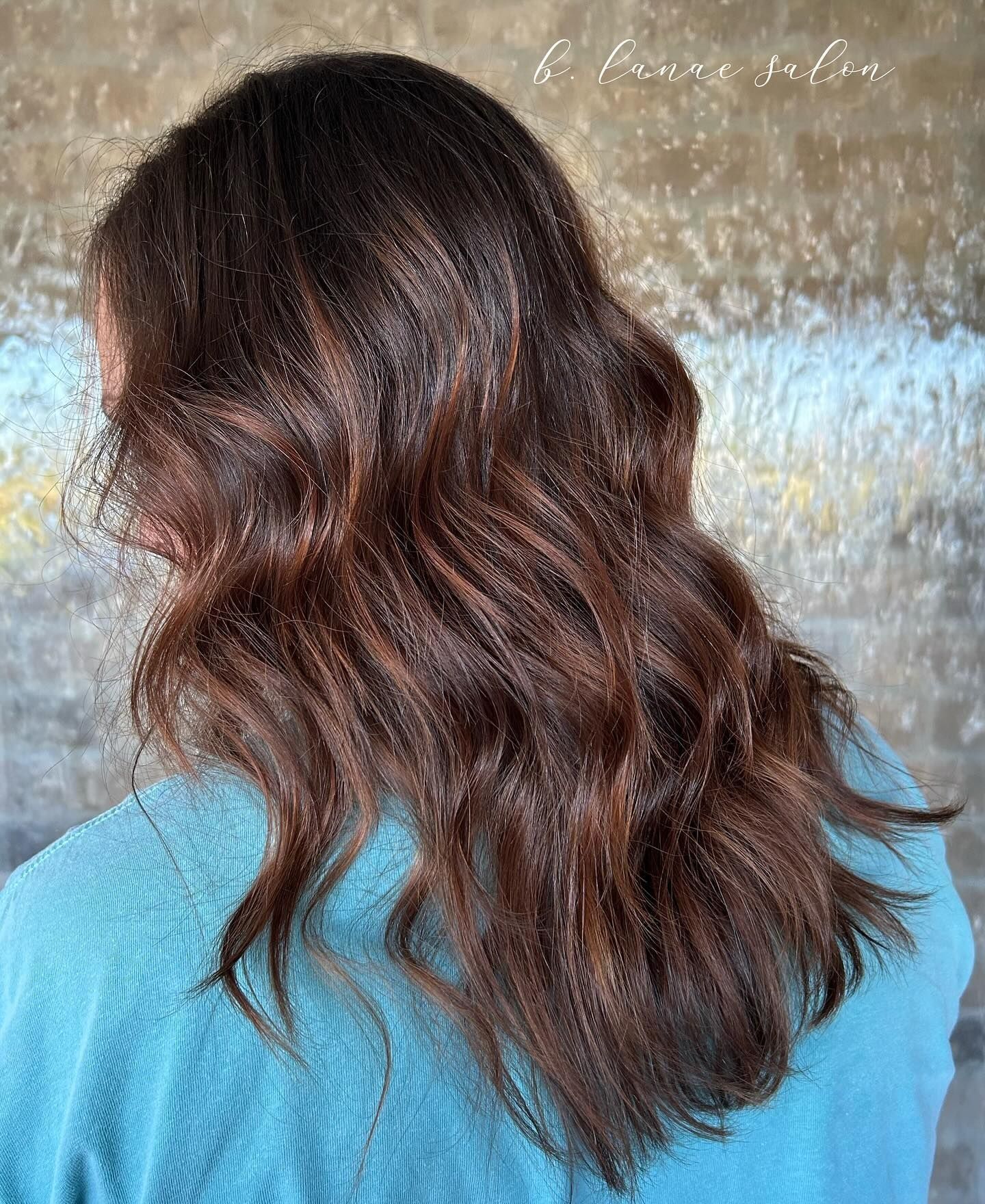 Woman with dark brown wavy hair, wearing a turquoise shirt, against a textured background.