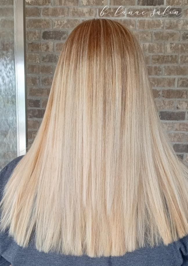 Blonde hair with ombre effect, styled straight. A brick wall is in the background.