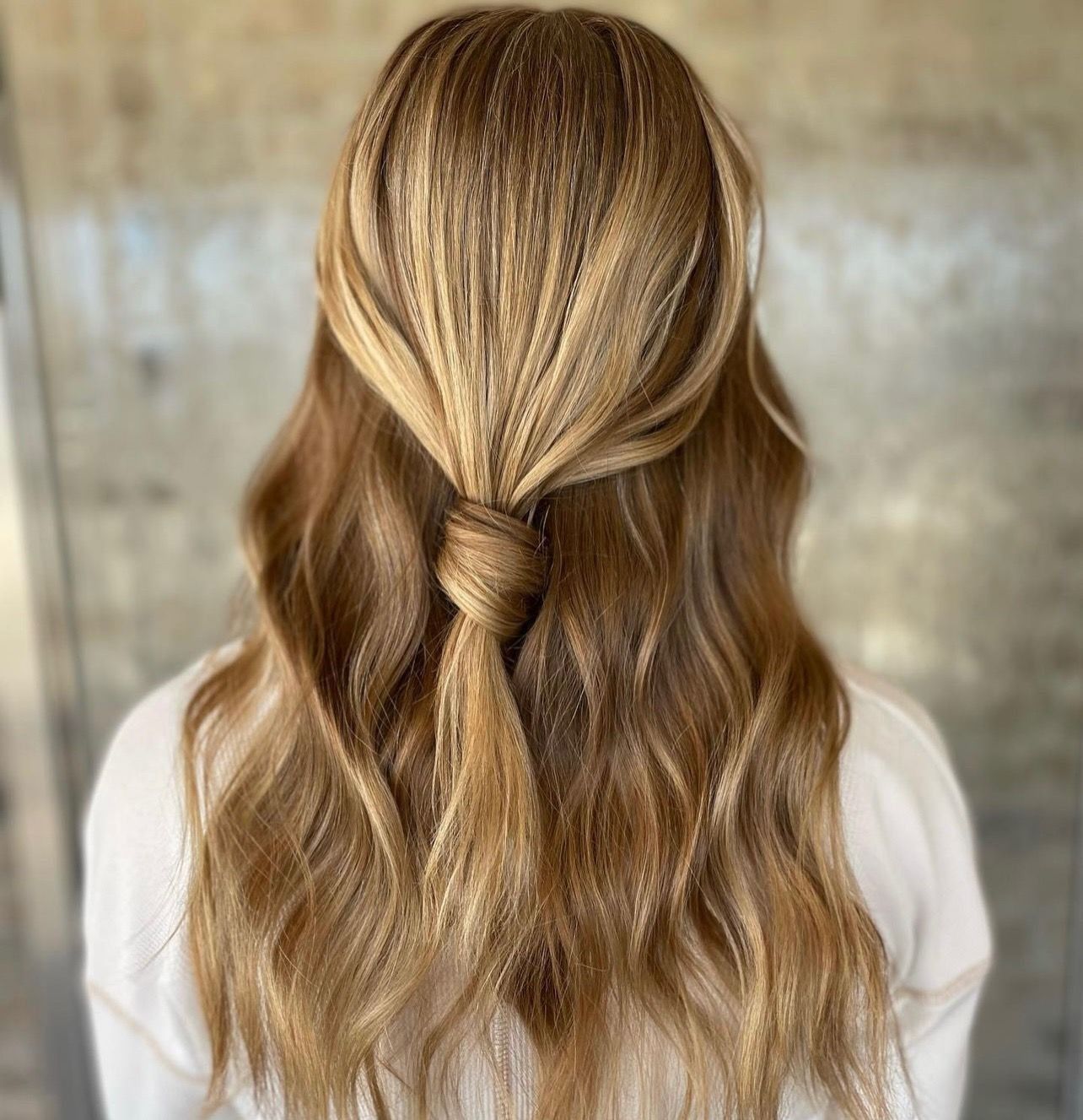 Woman with light brown, crimped hair pulled back in a knotted half-up style.