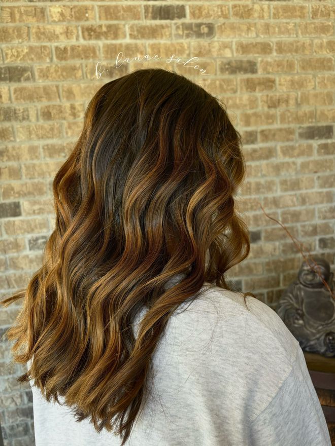 Woman with wavy brown hair, slight highlights, against a brick wall.