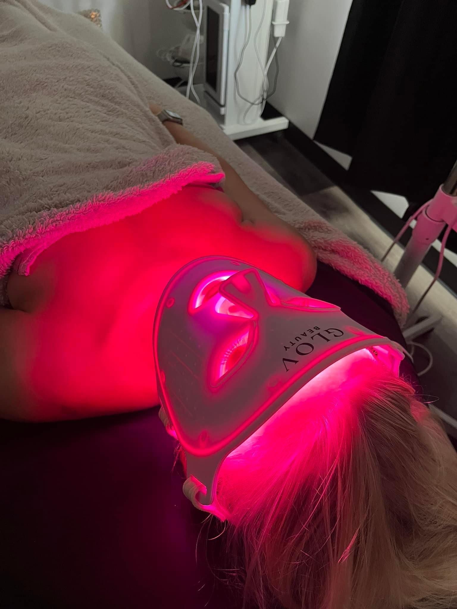 Person receiving red light therapy on face and neck in spa setting.