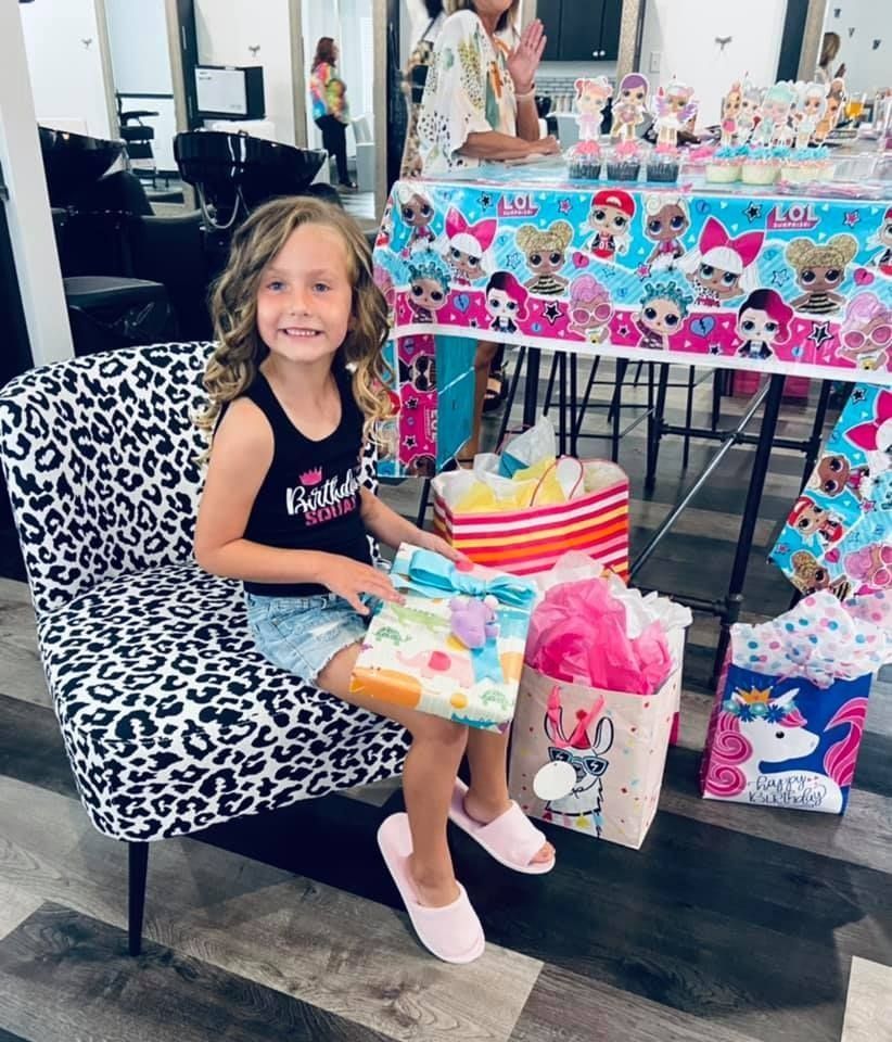 Girl sits on a leopard-print chair at an LOL doll party, smiling and holding a gift.