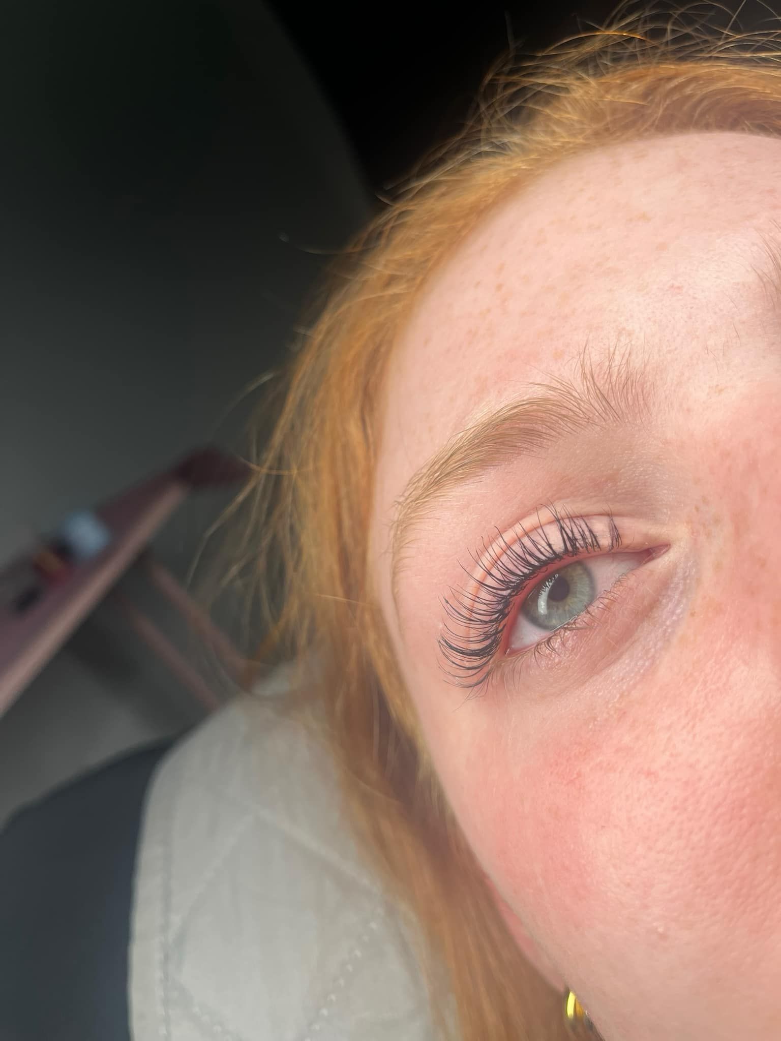 Close-up of a person's eye with red hair and pale skin. Lashes have dark mascara, indoors.