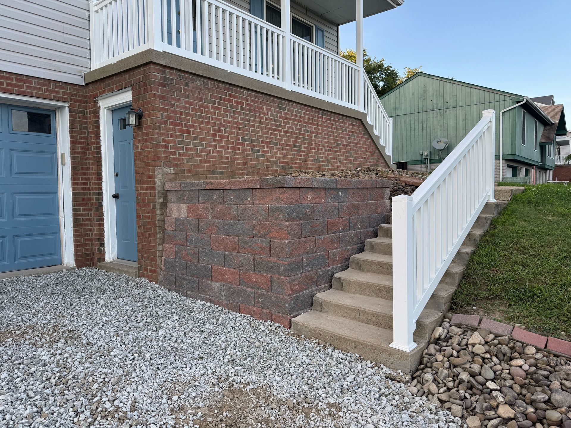Exterior of a house with steps, retaining wall, and blue garage door. White railing on steps and porch.