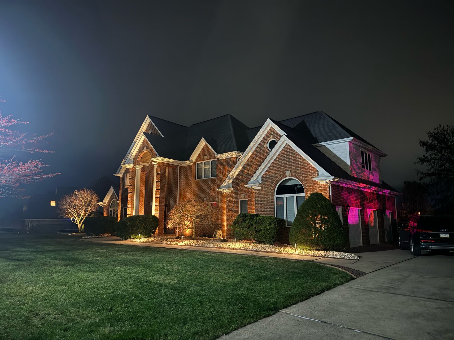 A large brick house is lit up at night with pink lights.
