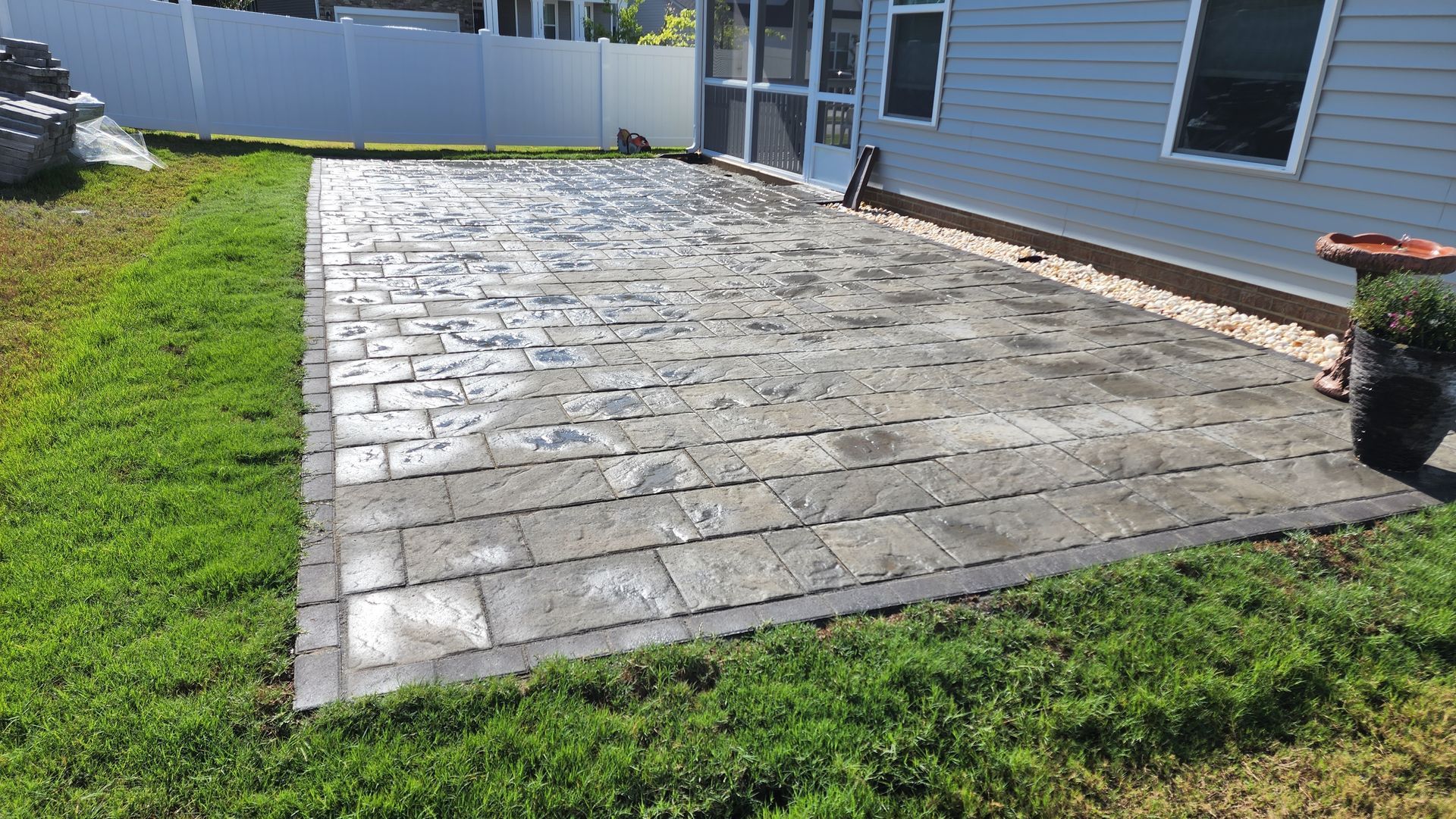 Paver patio with dark border next to a house with green grass on either side.