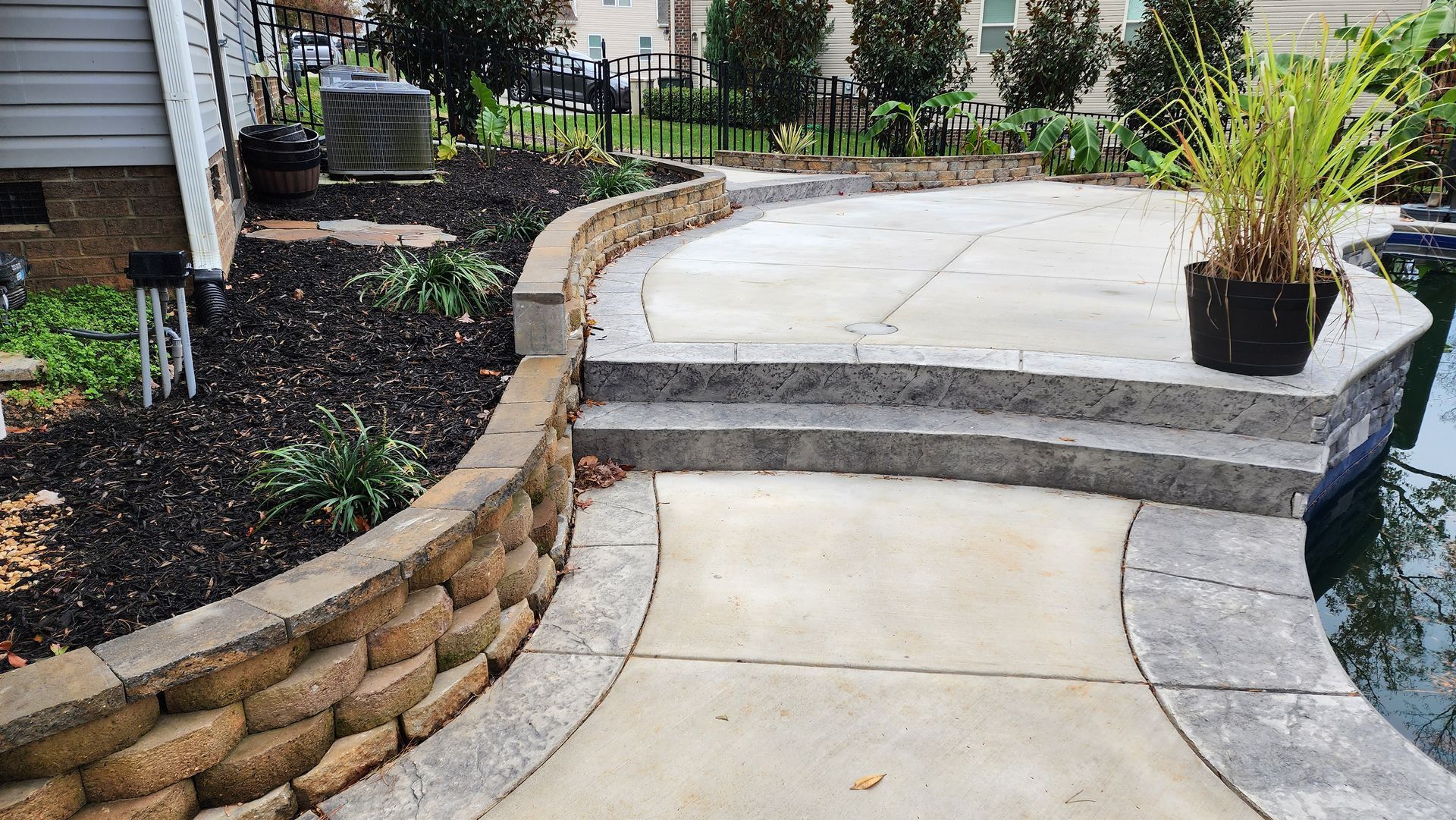 Stone patio with retaining wall and steps leading to a pool.