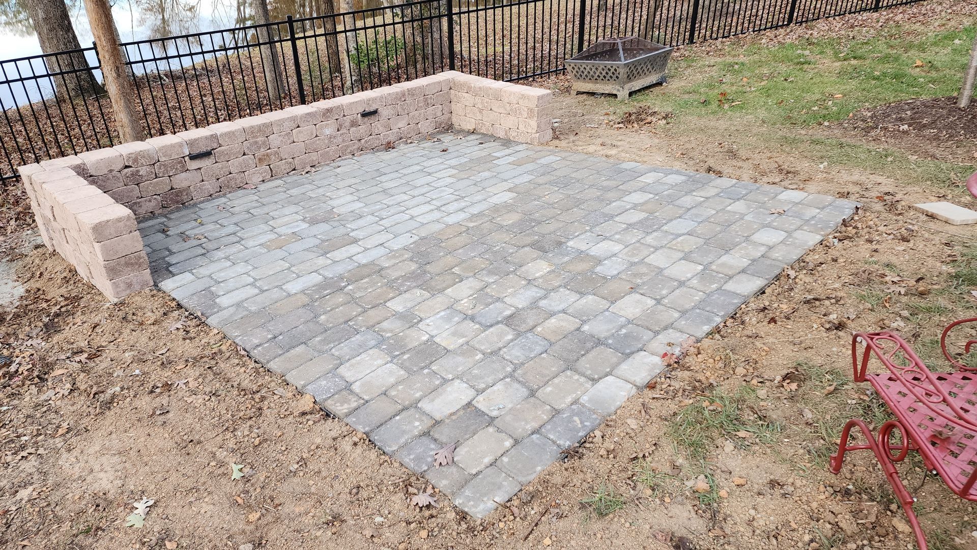 Brick patio with brick border, set in dirt near a fence and lake.