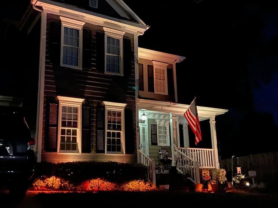 Two-story house at night, lit with orange lights and an American flag.