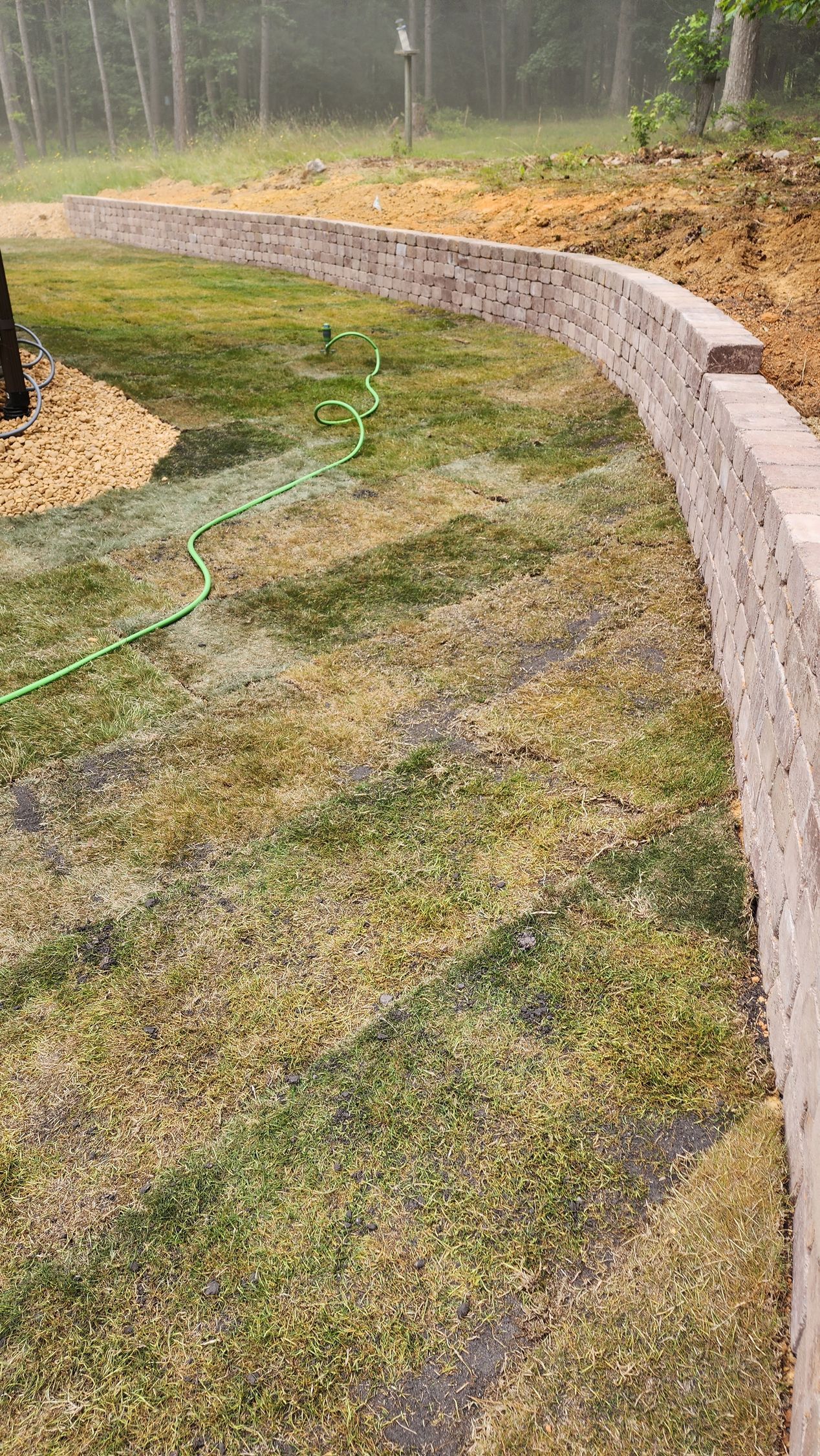Curving retaining wall built from blocks next to a patchy green lawn; dirt background.