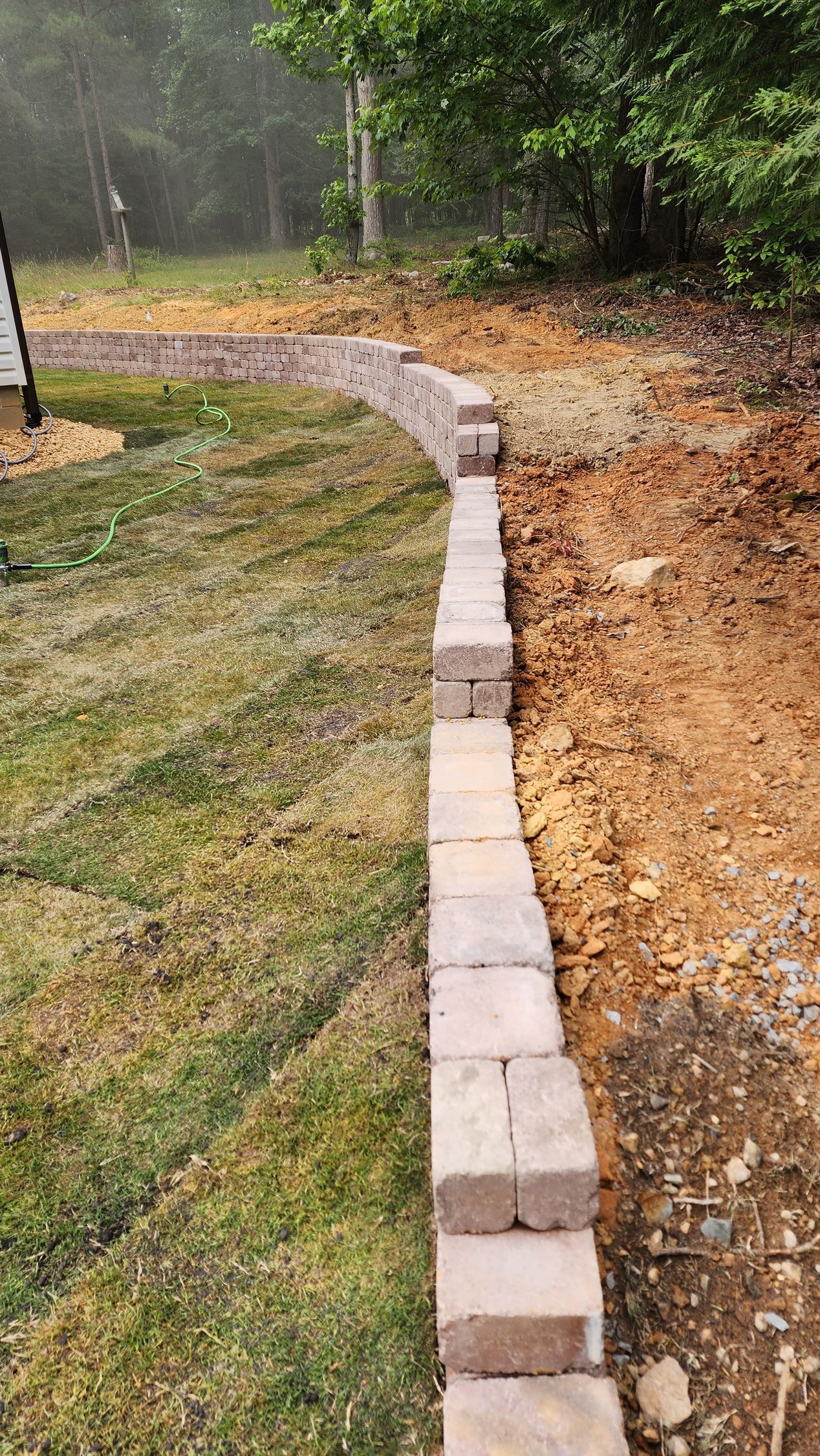 A low, curved brick retaining wall borders a grassy lawn and brown soil.