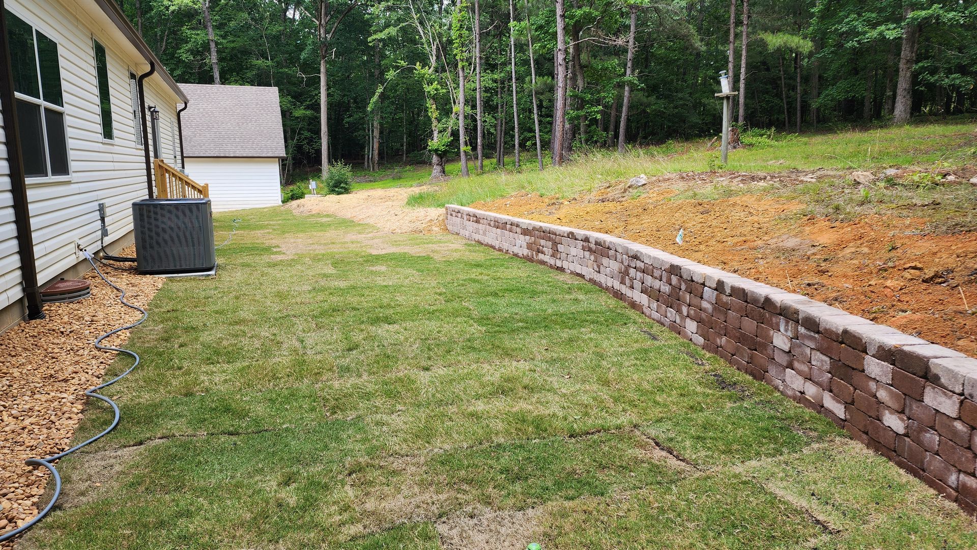Backyard with a brick retaining wall and a patch of grass near a house.
