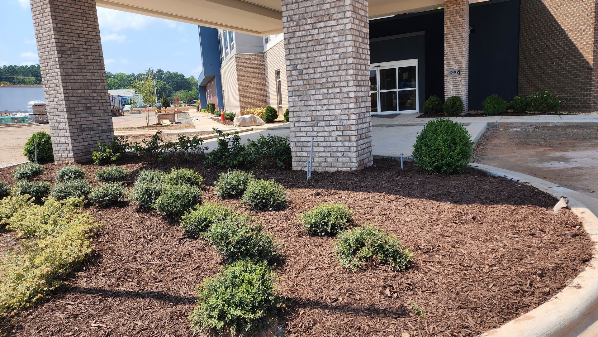 Entryway with stone columns, landscaping with mulch, green shrubs, and a hotel entrance.