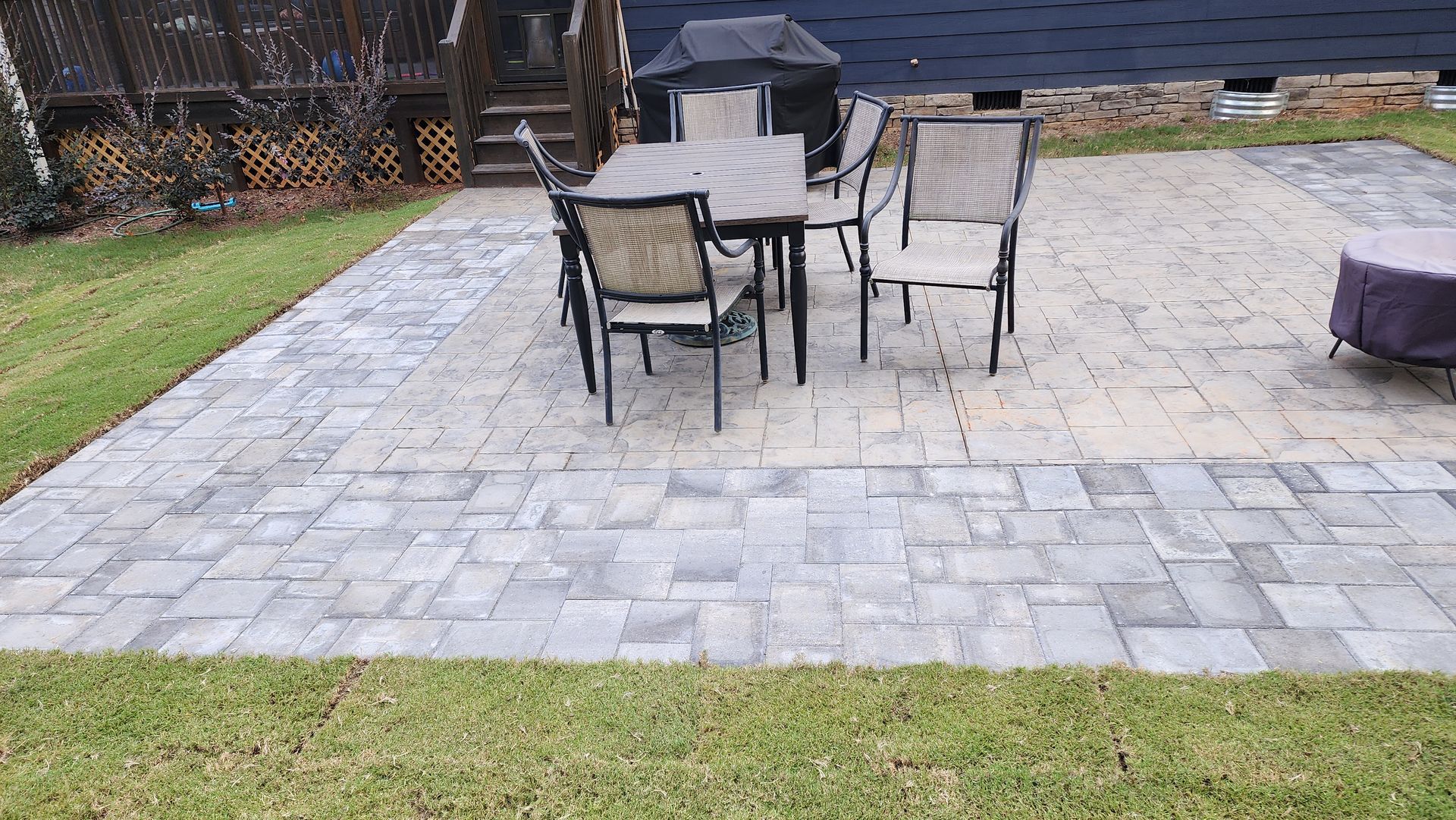 Patio with a table and chairs on pavers, surrounded by grass.