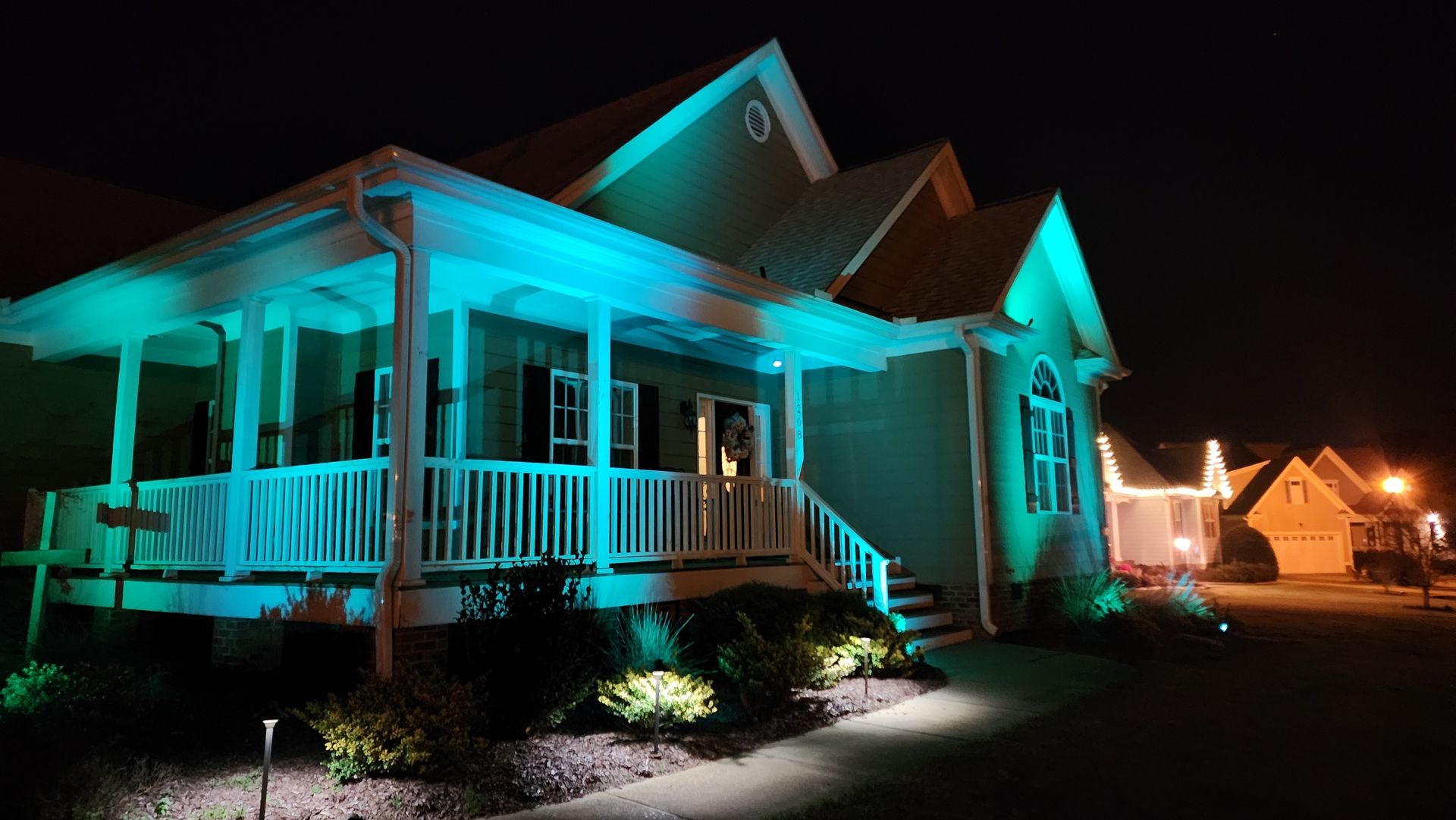 House with teal and green exterior lighting at night.