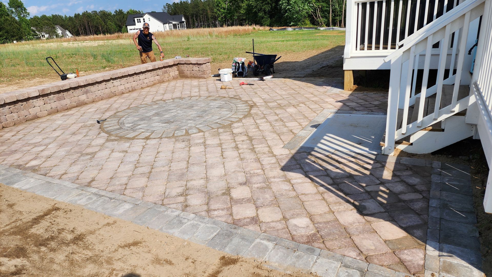 Brick patio with fire pit, next to a deck, and someone mowing the grass in the background.