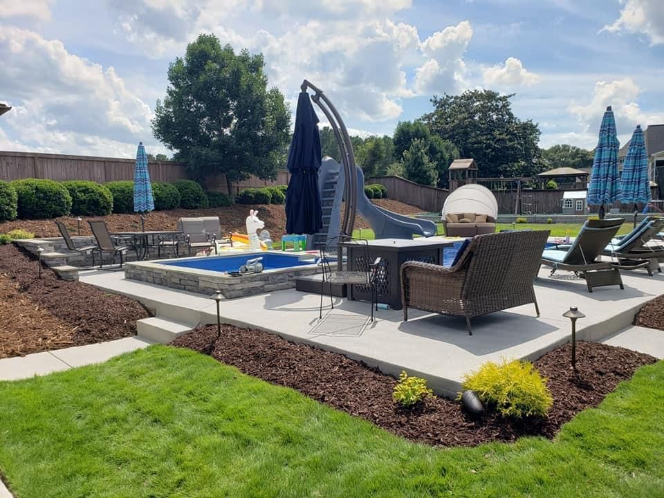 Backyard with pool, patio, chairs, and landscaping under a partly cloudy sky.