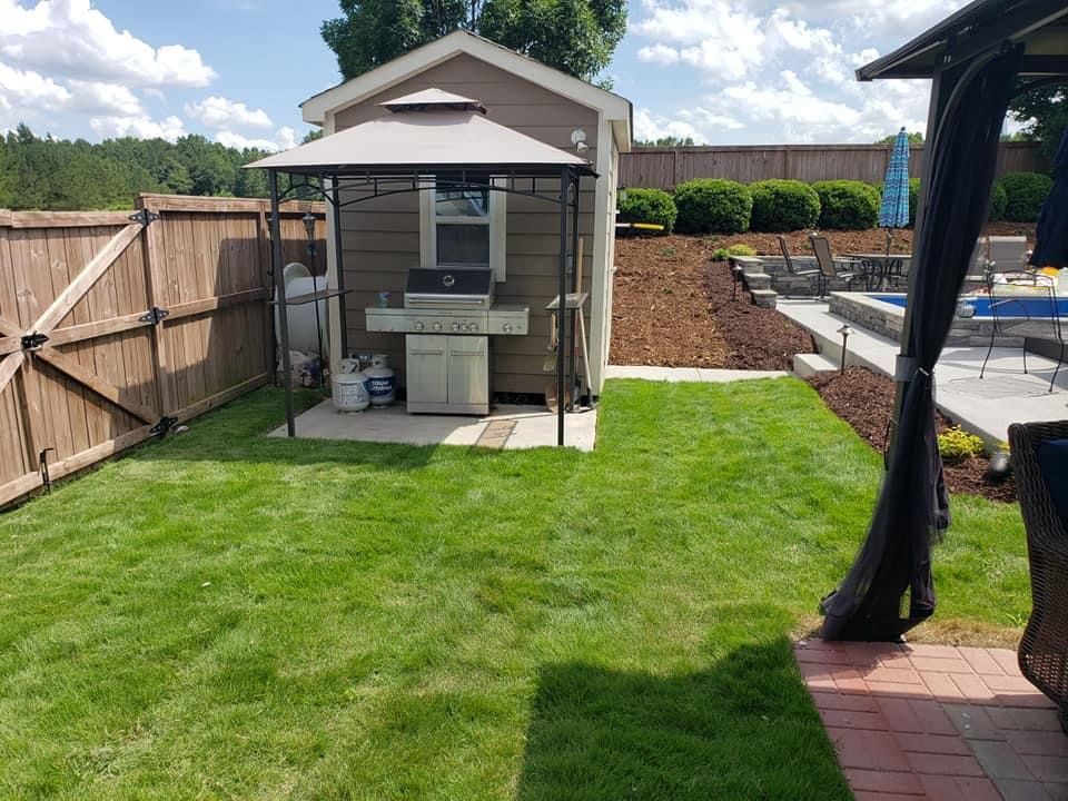 Backyard with a grilling station under a gazebo, near a fence and pool area.