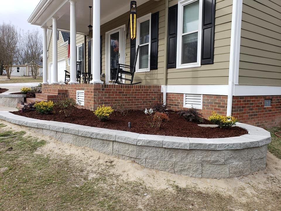 House with a curved retaining wall holding a flower bed, and a front porch with a brick base.