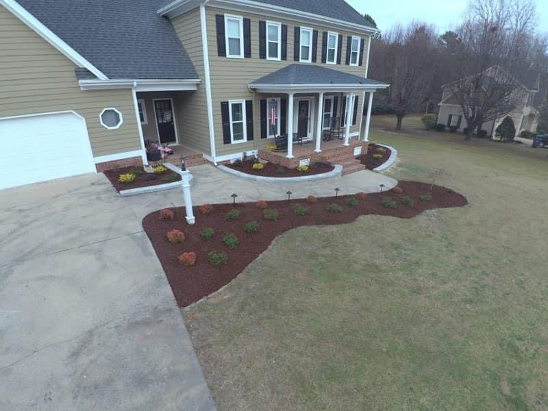 A two-story house with tan siding, black shutters, and landscaped front yard with a curved driveway.