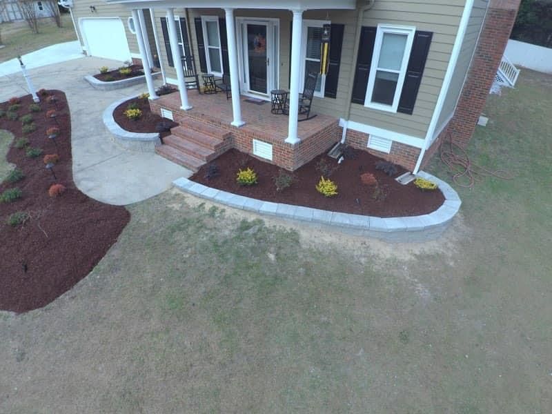 A house with a porch and landscaping, brown mulch, green grass, and a concrete driveway.
