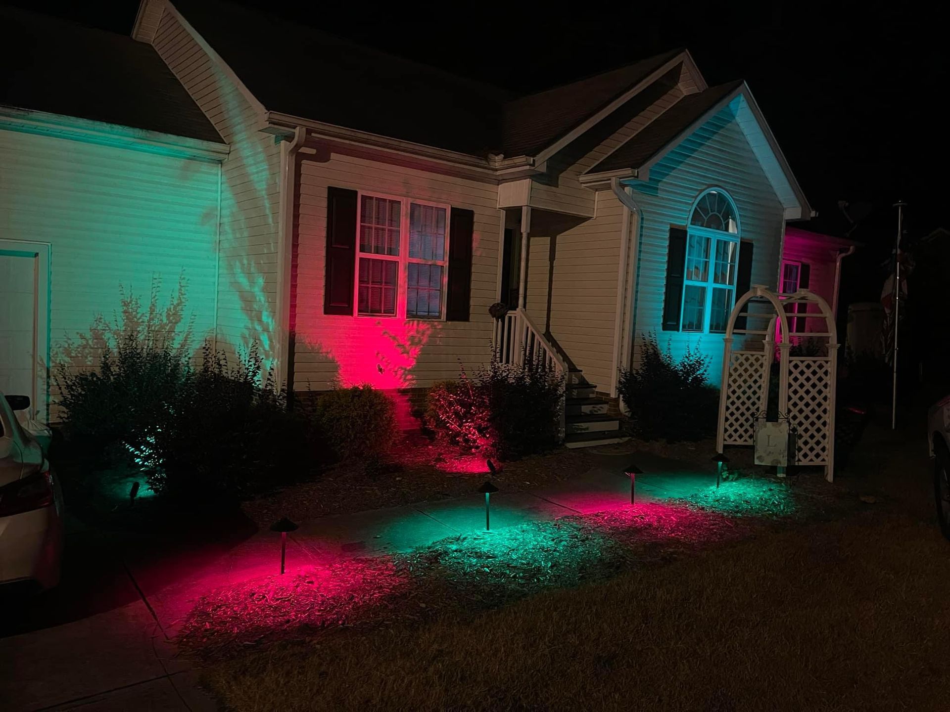 House illuminated at night with red and green landscape lights.