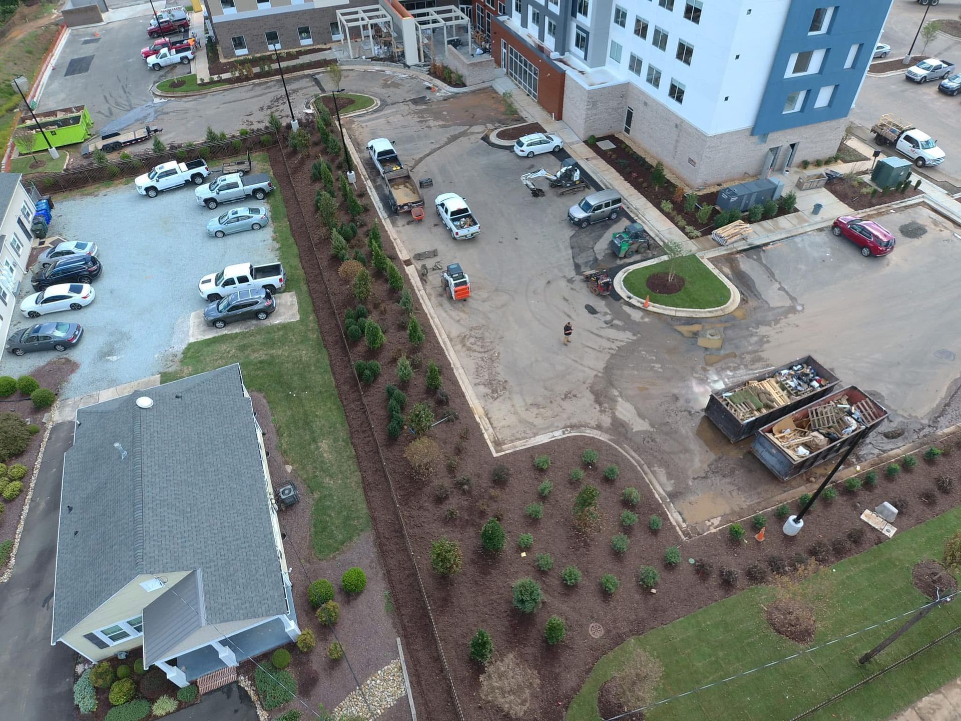 Aerial view of a construction site with parked cars, a building, and landscaping.