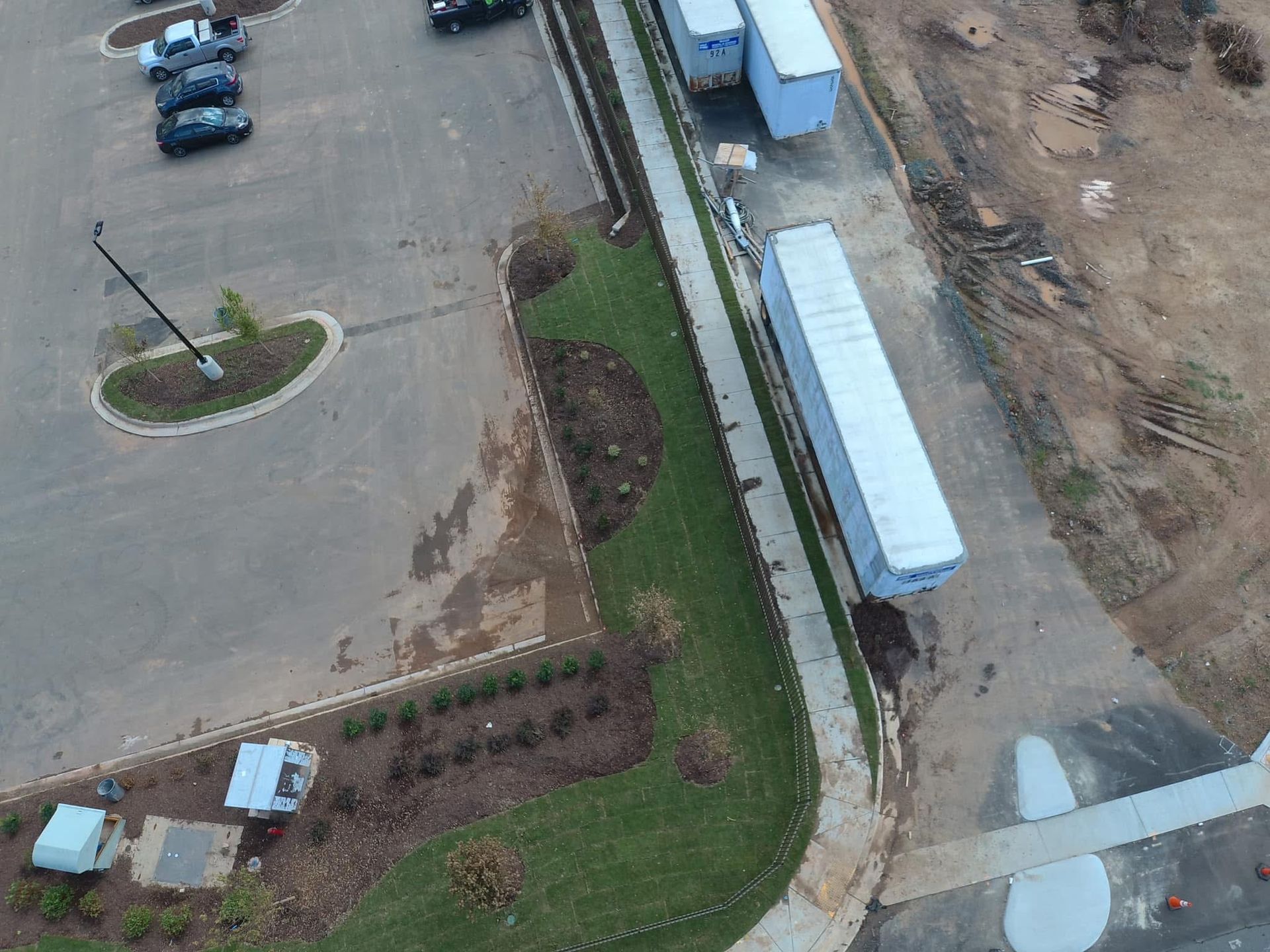 Aerial view of a parking lot, green landscaping, and semi-truck trailers alongside a sidewalk.