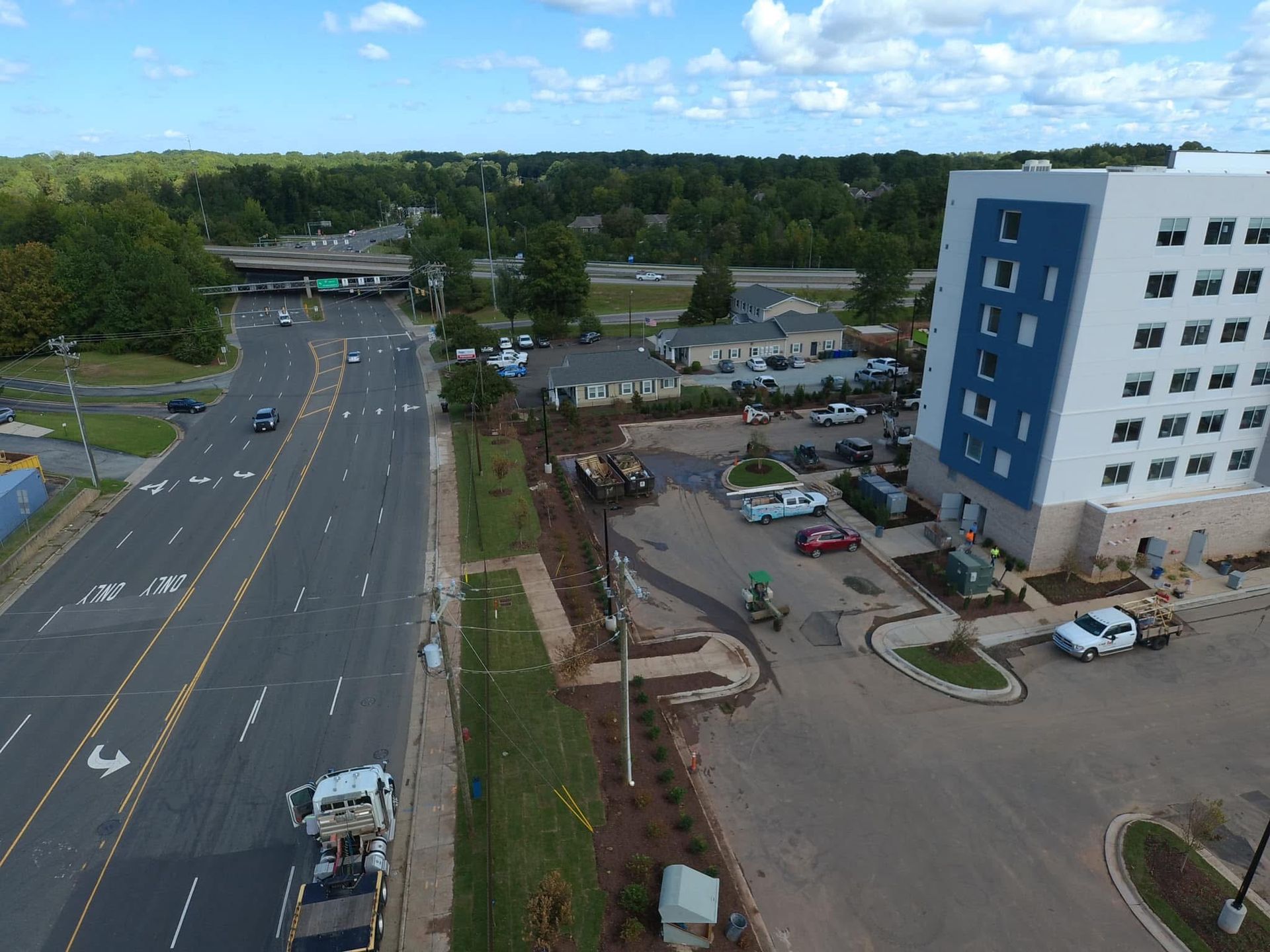 Aerial view of a multilane road next to a construction site near a tall white and blue building.
