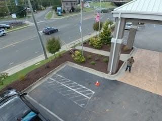 Person near hotel entrance, cars on street, green landscaping.
