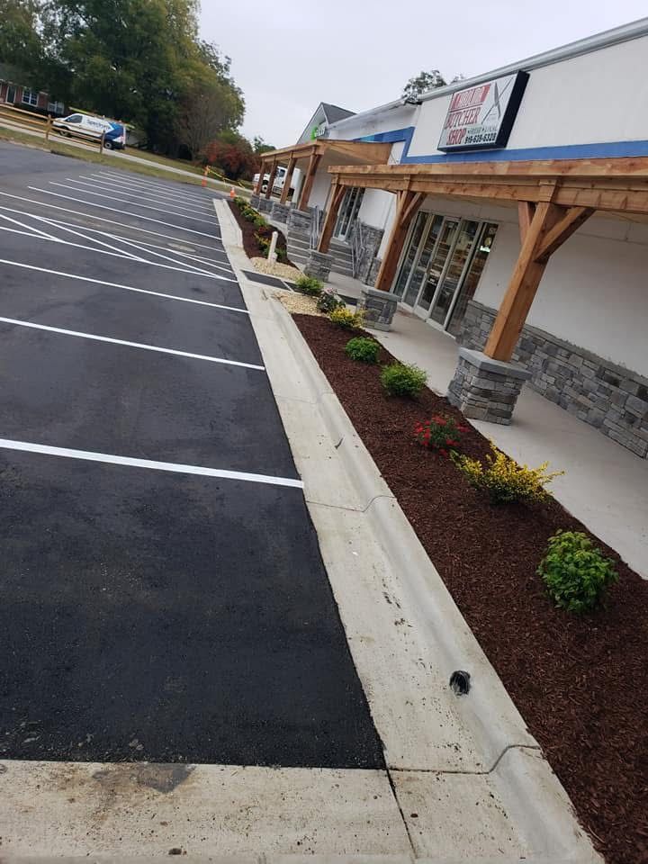 Exterior of commercial building with parking lot and landscaping. Asphalt, white lines, mulch, and plants visible.