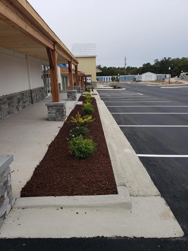 Exterior view of a commercial building with a planted bed filled with mulch and shrubs next to a parking lot.