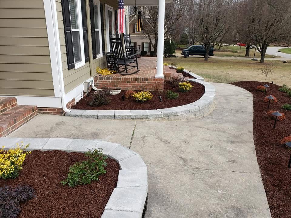 Curved concrete walkway leads to a house with a porch and flower beds.