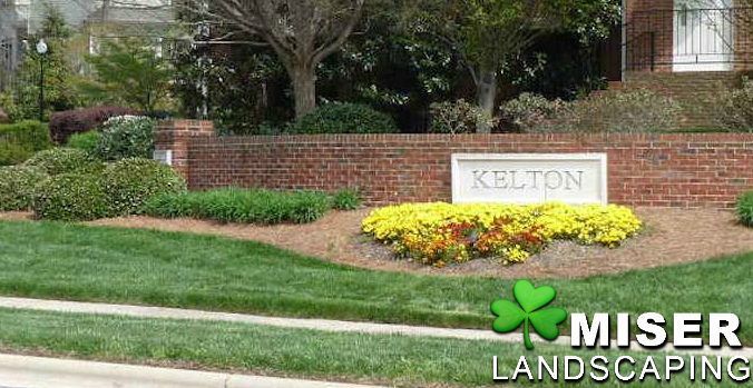 Sign for 'Kelton' in front of a brick wall, with landscaping and 'Miser Landscaping' logo.